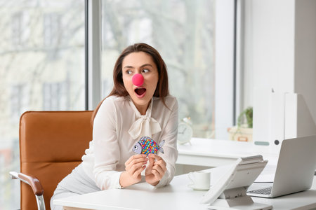 Funny young woman with clown nose and paper fish in office. april fools day celebrationの写真素材