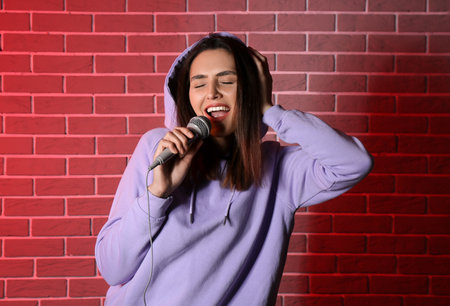 Cool young woman singing on color brick backgroundの写真素材
