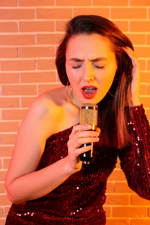 Pretty young singing woman with microphone on color brick background