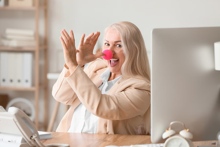 Funny mature woman with clown nose in office. april fools day celebrationの写真素材
