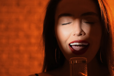 Pretty young singing woman with microphone on color backgroundの写真素材