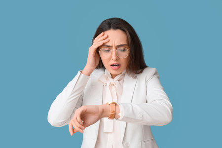 Portrait of worried young secretary looking at her watch on blue background