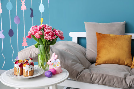 Easter cakes, eggs and rabbit with greeting card on table in room