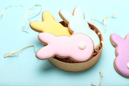 Box with delicious Easter cookies in shape of bunny on blue background, closeup
