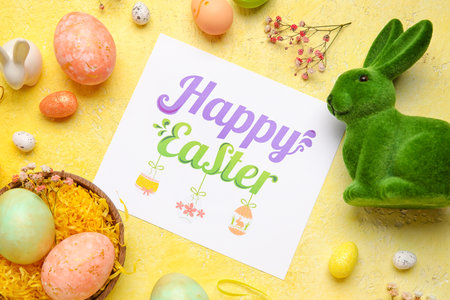 Beautiful Easter composition with greeting card, painted eggs, bunny and flowers on color background