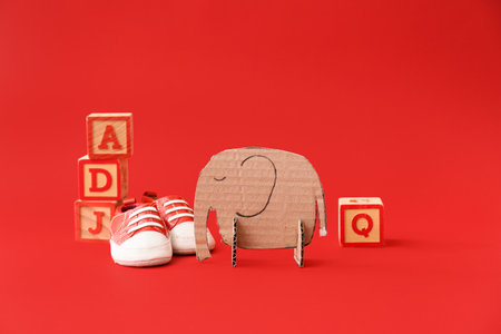 Handmade cardboard elephant, baby shoes and wooden cubes with letters on red background