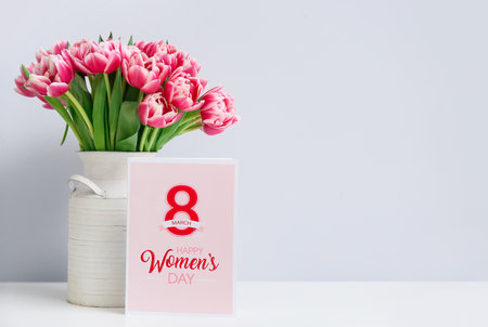 Beautiful bouquet of fresh flowers with greeting card on table in room. International Women's Day celebrationの写真素材