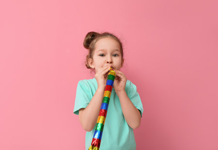 Funny little girl with party blower on color background. April fools' day celebrationの写真素材