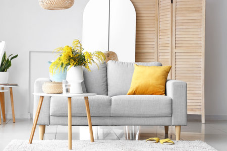 Vase with mimosa flowers on table and sofa in interior of living roomの写真素材