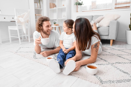 Young family with cups of tea resting on carpet at homeの写真素材