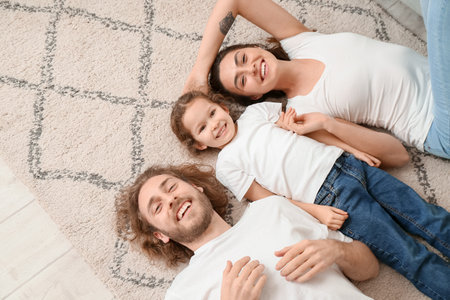 Happy young family lying on soft carpet at homeの写真素材