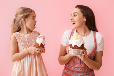 Little girl and her mother with tasty Easter cakes on pink backgroundの写真素材
