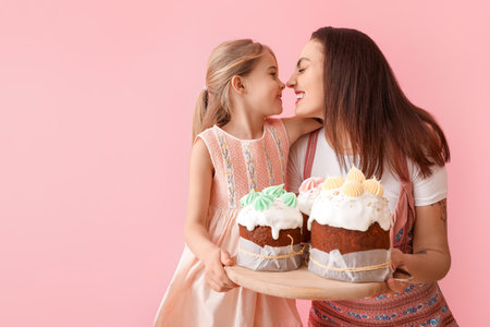 Little girl and her mother with tasty Easter cakes on pink background