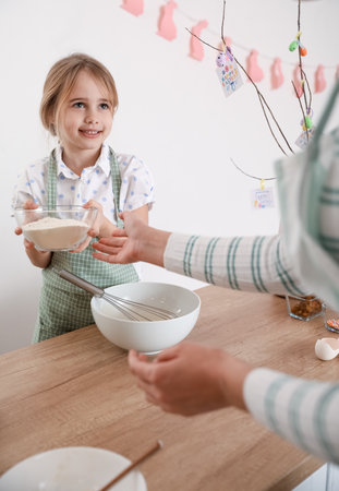 Little girl with her mother preparing dough for Easter cake in kitchen