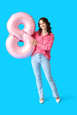 Smiling young woman with big balloon in shape of figure 8 on blue background. International Women's Dayの写真素材
