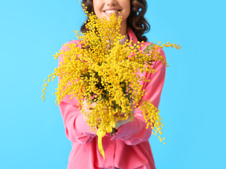 Young woman with mimosa flowers on blue background, closeup. International Women's Dayの写真素材