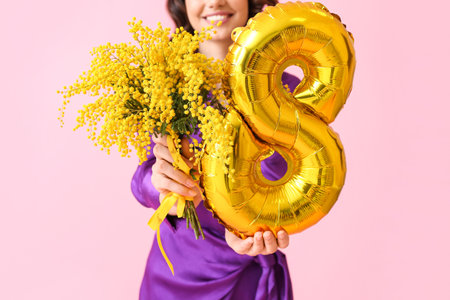 Young woman with mimosa flowers and balloon in shape of figure 8 on pink background. International Women's Dayの写真素材