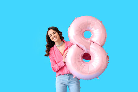 Smiling young woman with big balloon in shape of figure 8 on blue background. International Women's Dayの写真素材