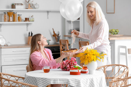 Mature woman greeting her daughter with balloons and eclairs in the kitchen on International Women's Dayの写真素材