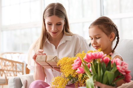 Young woman with her little daughter, gift and flowers at home on holidayの写真素材