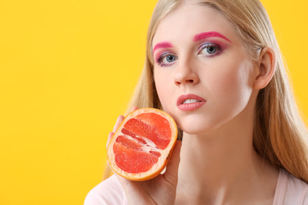 Portrait of woman with extraordinary makeup holding grapefruit on color backgroundの写真素材