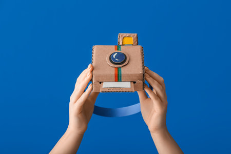 Female hands with cardboard photo camera on color backgroundの写真素材
