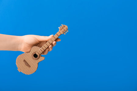 Female hand with cardboard guitar on color backgroundの写真素材