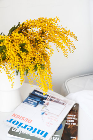 Vase with mimosa flowers and magazines on bedside table near light wall, closeupの写真素材
