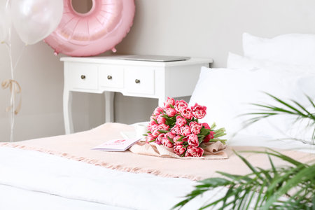 Bouquet of tulips and greeting card on bed in room. International Woman's Day celebrationの写真素材