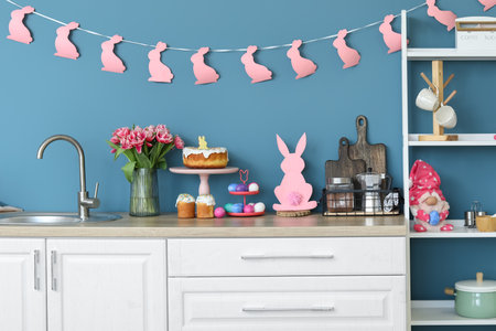 Stand with cake and Easter eggs on counter near color wall in kitchen interiorの写真素材