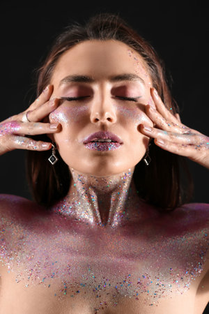 Beautiful young woman with glitters on her face and body against dark backgroundの写真素材
