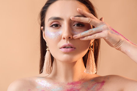 Beautiful young woman with glitters on her face and body against color background