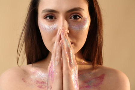 Beautiful young woman with glitters on her face and body against color background