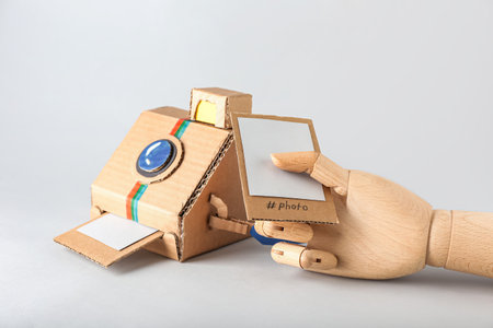 Cardboard photo camera and wooden hand with picture on light background