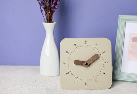 Alarm clock, photo frame and vase with lavender flowers on table near color wall