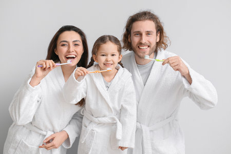 Little girl with her parents brushing teeth on light backgroundの写真素材