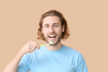 Young man brushing teeth on beige background, closeupの写真素材