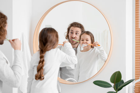 Little girl with her father brushing teeth near mirror in bathroomの写真素材