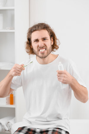 Emotional young man with toothbrush and paste in bathroom