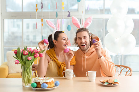 Happy couple in bunny ears with Easter eggs sitting at table