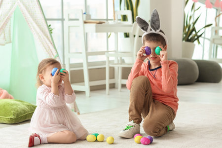 Cute little children in bunny ears with Easter eggs at home