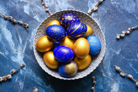 Basket with stylish Easter eggs and willow branches on blue background