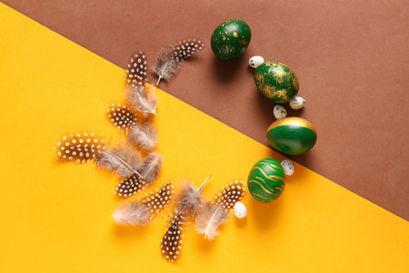 Frame made of stylish Easter eggs and feathers on color background