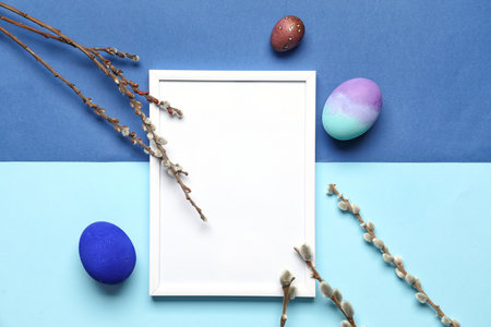 Easter composition with blank photo frame, eggs and willow branches on blue backgroundの写真素材