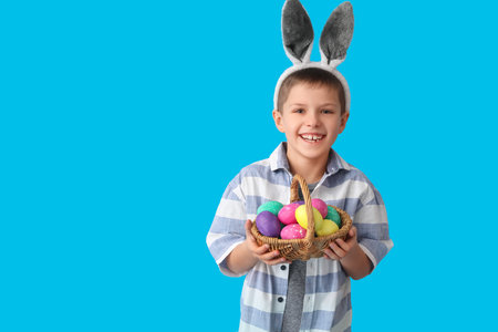 Funny little boy with bunny ears and Easter basket on blue backgroundの写真素材