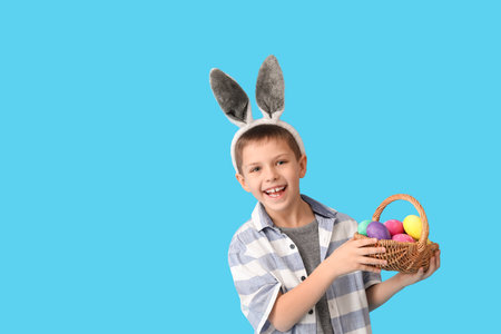 Funny little boy with bunny ears and Easter basket on blue backgroundの写真素材