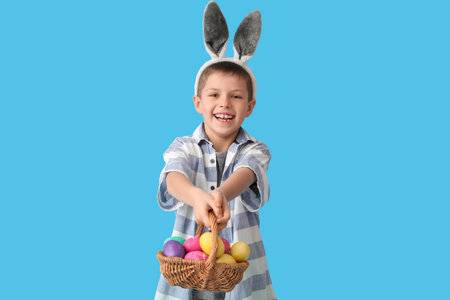 Funny little boy with bunny ears and Easter basket on blue background