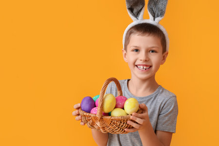 Funny little boy with bunny ears and Easter basket on yellow background