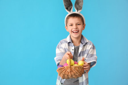 Funny little boy with bunny ears and Easter basket on blue backgroundの写真素材
