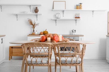 Dining table with pumpkins, pampas grass and burning candles in light kitchenの写真素材